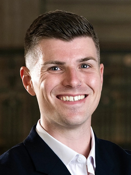 A white man with short dark hair wearing a white button-down shirt and a dark sports jacket.