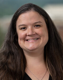 A white woman with long dark hair wearing a necklace and a black blouse.