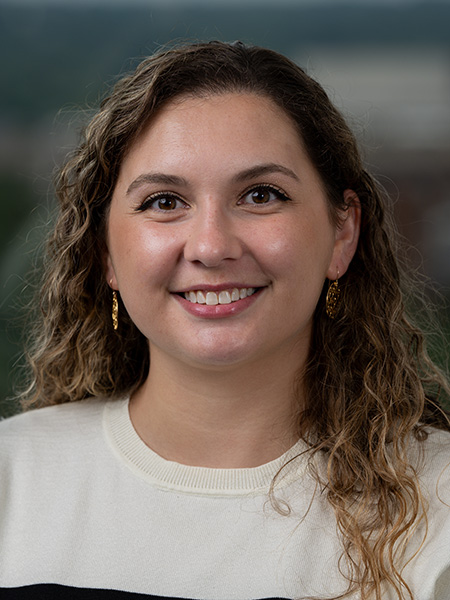 A white woman with long, curly blone hair wearing a white sweater and gold earrings.