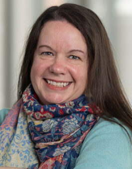A white woman with dark long hair wearing a multi-colored teal and teal sweater