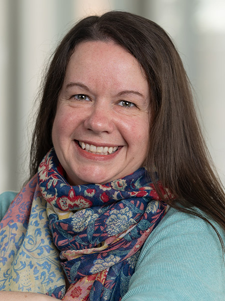 A white woman with dark long hair wearing a multi-colored teal and teal sweater