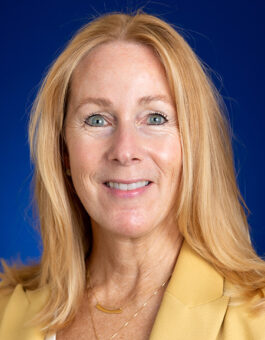 A white woman with long blonde hair wearing gold necklaces and a yellow blazer.