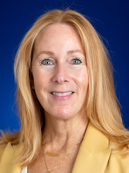 A white woman with long blonde hair wearing gold necklaces and a yellow blazer.