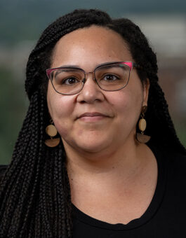 A black woman with long boxbraids weating a black sweater and geometric earrings.