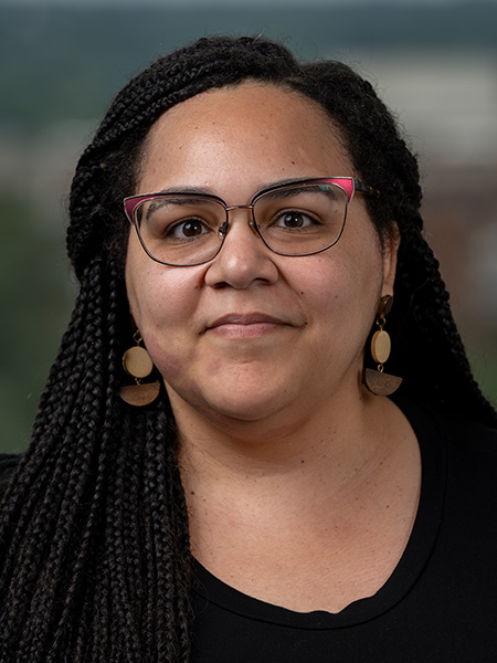 A black woman with long boxbraids weating a black sweater and geometric earrings.