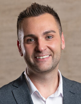 A white man with short spiky brown hair in a white button-down and gray sports coat.