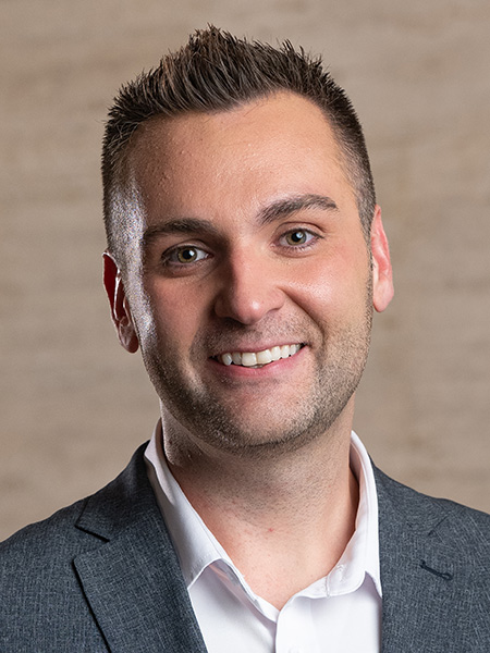 A white man with short spiky brown hair in a white button-down and gray sports coat.