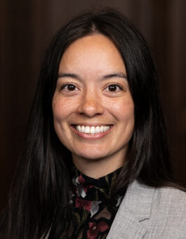 Woman with long dark hair wearing a dark floral buttondown and a gray blazer.