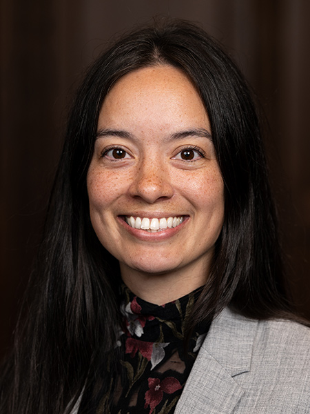Woman with long dark hair wearing a dark floral buttondown and a gray blazer.