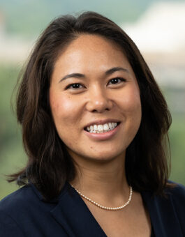 An asian woman with dark shoulder length hair wearing a small pear necklace and a dark blazer.