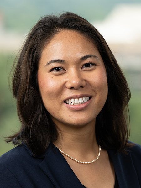 An asian woman with dark shoulder length hair wearing a small pear necklace and a dark blazer.