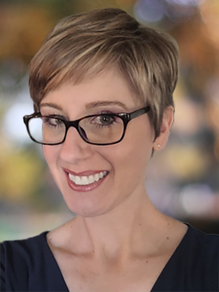 A white woman with short blonde hair wearing glasses and a dark shirt.
