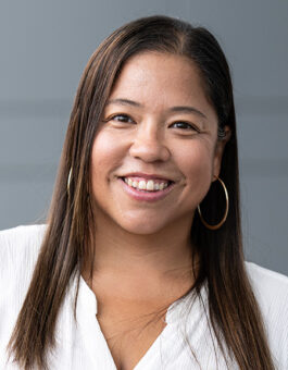 A woman with long dark hair wearing large gold earrings and a white shirt.