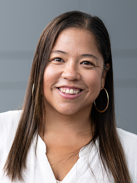 A woman with long dark hair wearing large gold earrings and a white shirt.