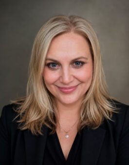 A white woman with shoulder length blonde hair is a black suite jacket and blouse.