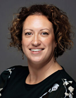 A woman with chin length curly hair wearing a black floral blouse.