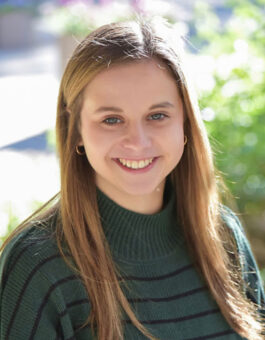 White woman with long blonde hair in a green and black striped sweater.