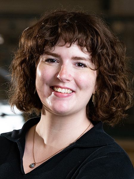 A white woman with a auburn, curly bob wearing a dark blouse and a necklace.