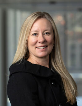 A white woman with long blonde hair in a black suit jacket.