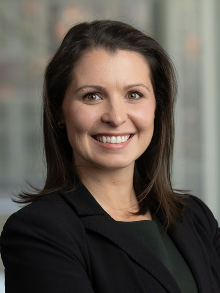 White woman with long dark hair and wearing a dark shirt and blazer.