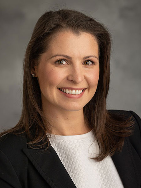 White woman with long dark hair and wearing a white shirt and dark blazer.