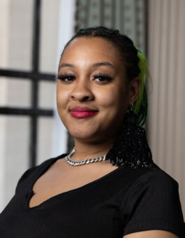 A woman with box braids pulled back and a black shirt on.