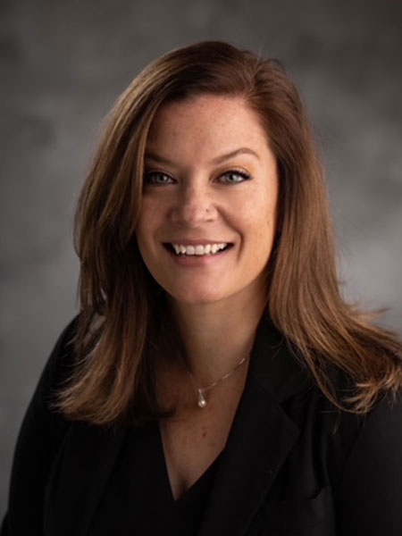 White woman with long brown hair and wearing a dark shirt and gold necklace.