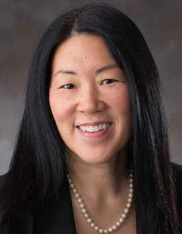 An asian woman with long dark hair wearing a pearl necklace and black blouse.