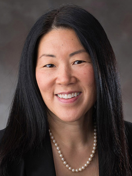 An asian woman with long dark hair wearing a pearl necklace and black blouse.