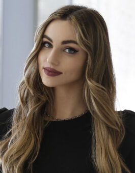A white woman with long highlighted hair wearing a black blouse.